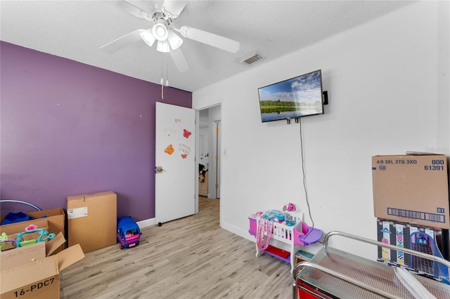 playroom with ceiling fan, a textured ceiling, and light wood-type flooring