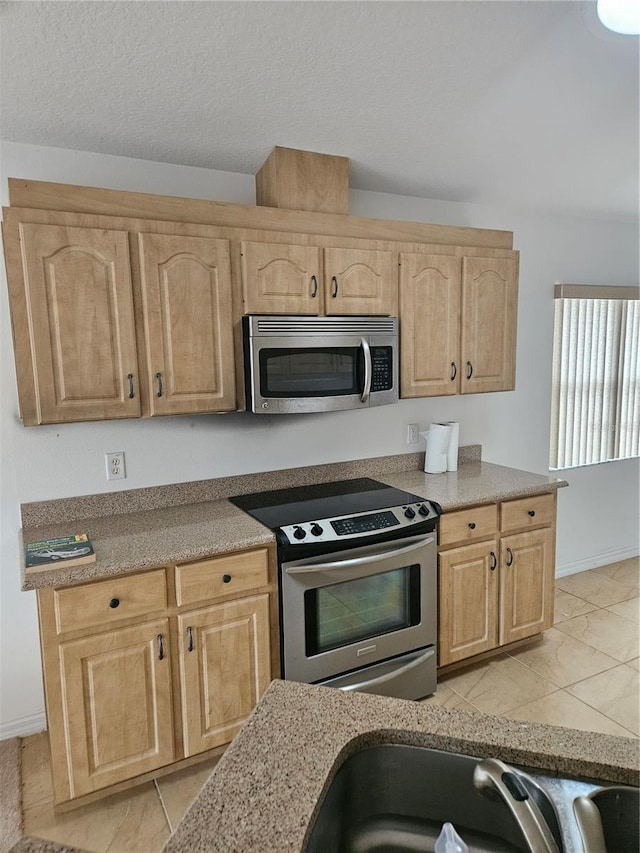 kitchen with light brown cabinets, baseboards, a sink, stainless steel appliances, and a textured ceiling