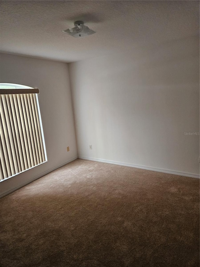 unfurnished room with light colored carpet, baseboards, and a textured ceiling