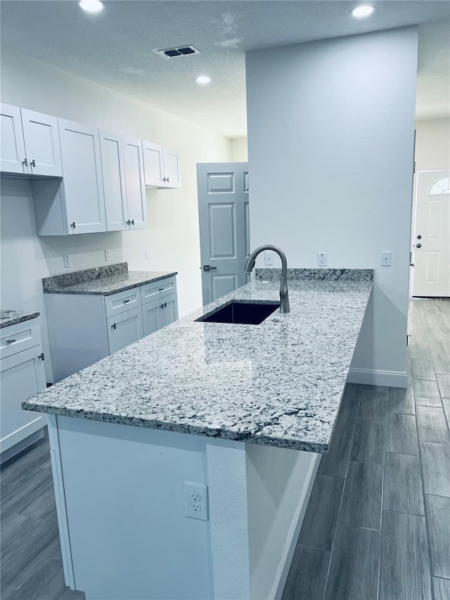 kitchen with white cabinets, light stone counters, a peninsula, wood tiled floor, and a sink