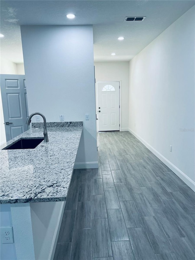 kitchen with light stone counters, a sink, visible vents, baseboards, and wood tiled floor