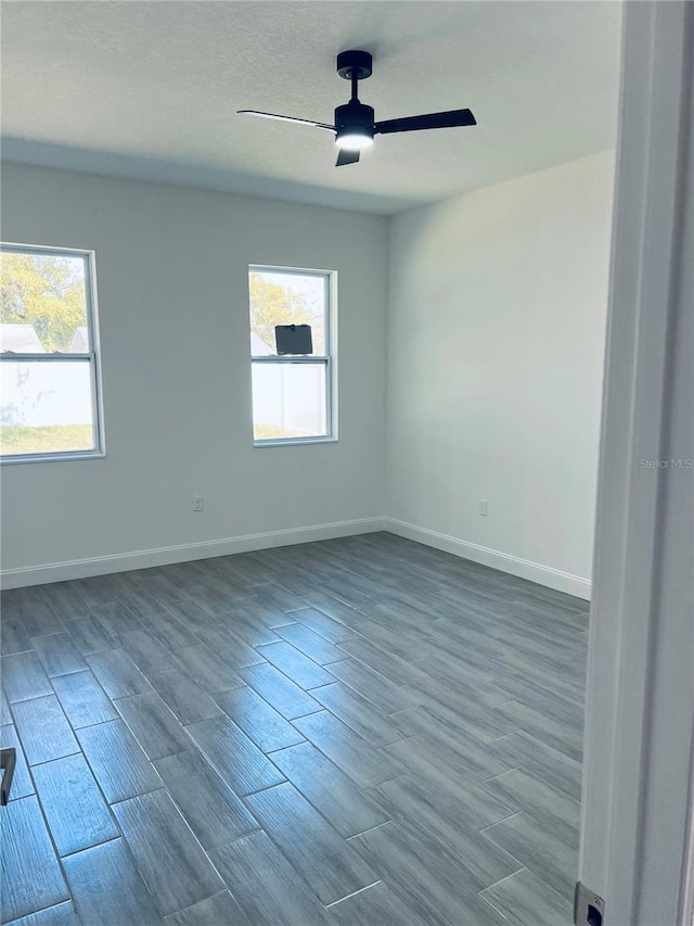 empty room with a healthy amount of sunlight, ceiling fan, baseboards, and wood finished floors