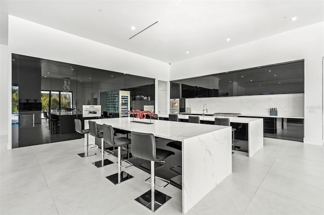 kitchen with sink, backsplash, a kitchen bar, stainless steel oven, and a spacious island