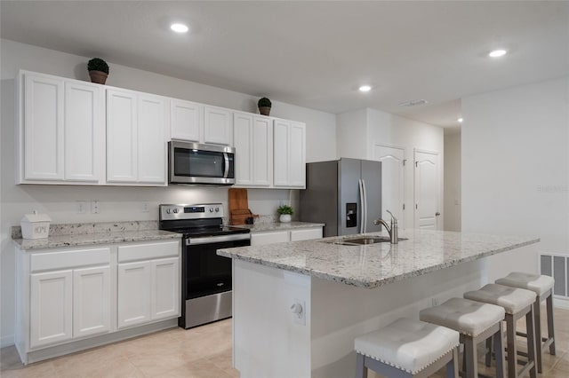 kitchen with appliances with stainless steel finishes, an island with sink, a sink, and white cabinetry