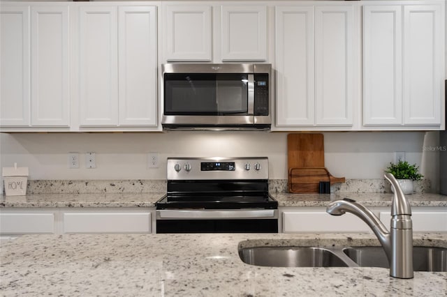 kitchen featuring stainless steel appliances, white cabinets, a sink, and light stone counters