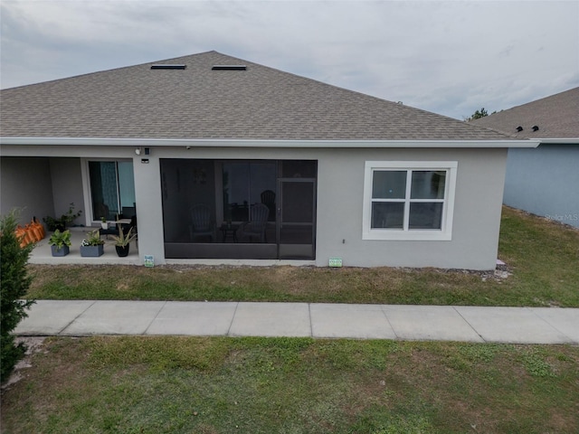 rear view of property featuring a sunroom, roof with shingles, a lawn, and stucco siding