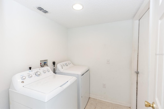 clothes washing area featuring separate washer and dryer, a textured ceiling, and light tile patterned flooring