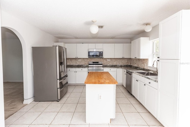 kitchen with sink, white cabinetry, stainless steel appliances, a kitchen island, and wood counters