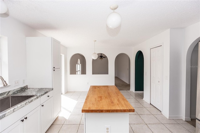 kitchen featuring wood counters, decorative light fixtures, white cabinetry, sink, and a center island