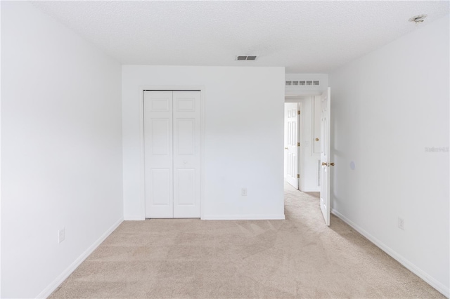 unfurnished bedroom with light colored carpet, a closet, and a textured ceiling