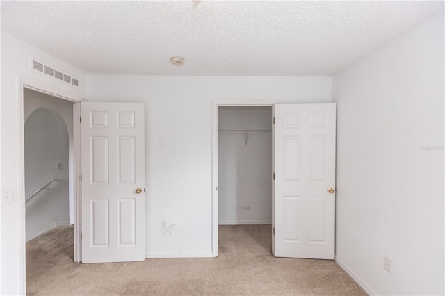 unfurnished bedroom featuring a spacious closet, light colored carpet, a textured ceiling, and a closet