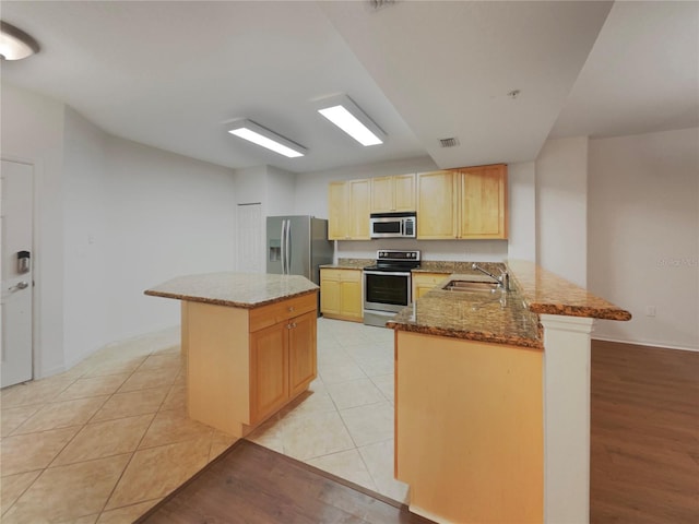 kitchen featuring sink, stainless steel appliances, light stone countertops, light tile patterned flooring, and kitchen peninsula