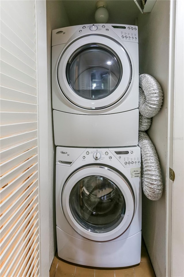 laundry area with light tile patterned flooring and stacked washing maching and dryer