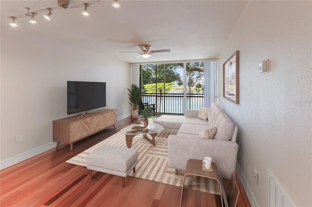 living room featuring expansive windows, ceiling fan, wood-type flooring, and rail lighting