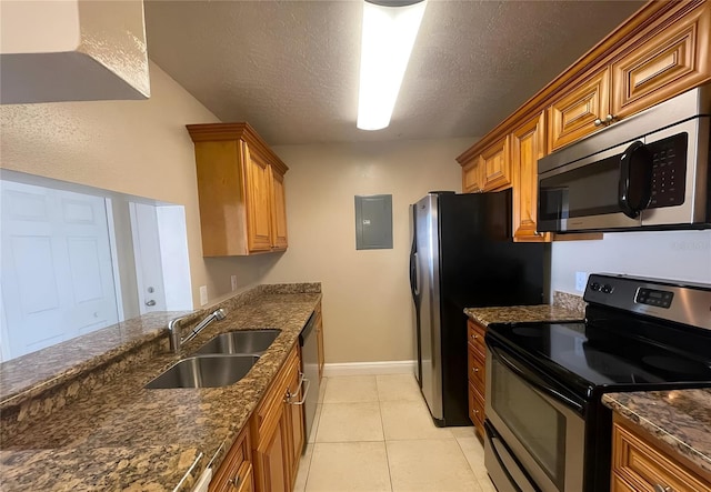 kitchen with sink, light tile patterned floors, stainless steel appliances, a textured ceiling, and dark stone counters