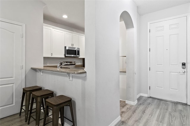 kitchen featuring appliances with stainless steel finishes, white cabinetry, a kitchen breakfast bar, light stone counters, and light hardwood / wood-style floors