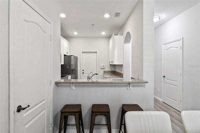 kitchen featuring white cabinetry, stainless steel refrigerator, kitchen peninsula, and a breakfast bar