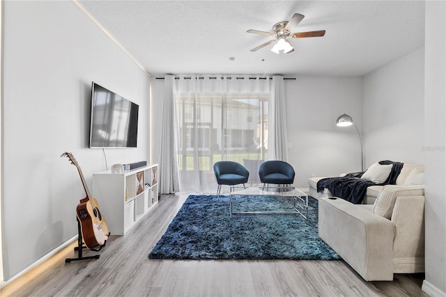 living room featuring ceiling fan, a textured ceiling, and light wood-type flooring