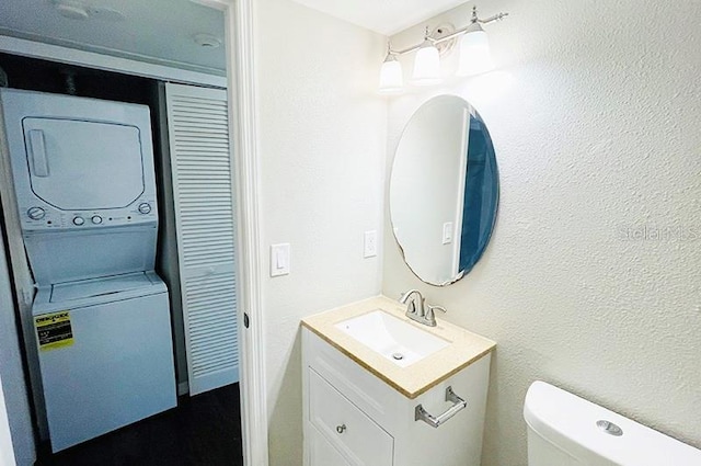 bathroom featuring vanity, stacked washer and clothes dryer, and toilet