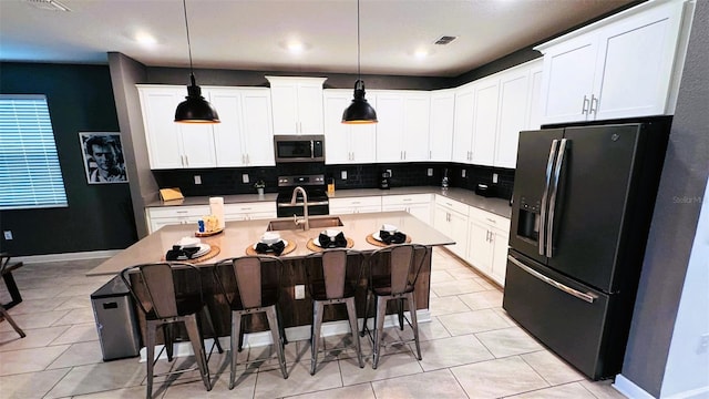 kitchen featuring white cabinetry, a center island with sink, a breakfast bar area, and black fridge