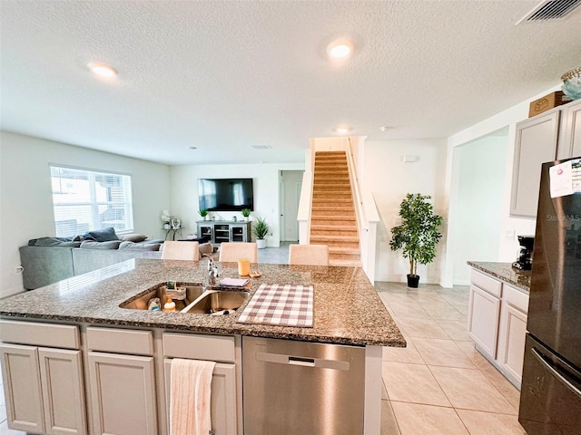 kitchen featuring light tile patterned flooring, an island with sink, sink, light stone counters, and stainless steel appliances