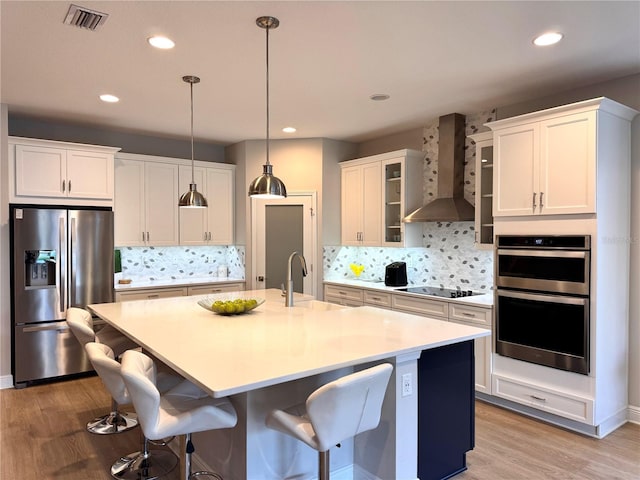 kitchen featuring stainless steel appliances, sink, a center island with sink, and wall chimney exhaust hood