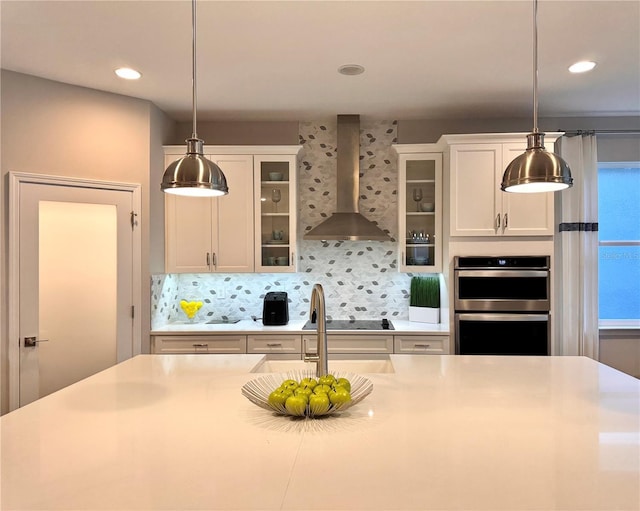 kitchen featuring white cabinetry, double oven, decorative light fixtures, and wall chimney exhaust hood