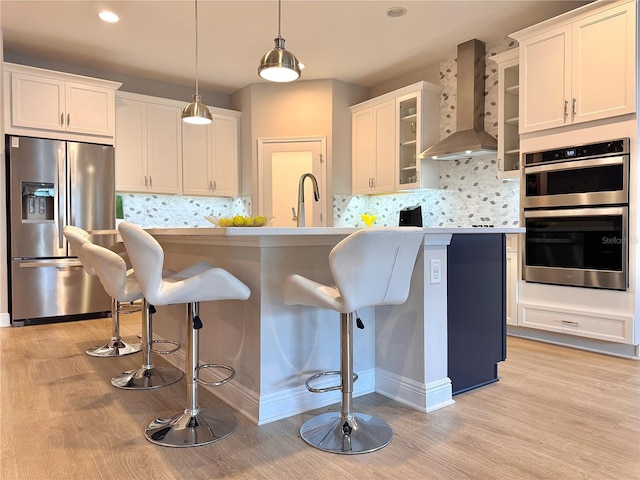 kitchen featuring white cabinetry, a breakfast bar area, hanging light fixtures, stainless steel appliances, and wall chimney range hood