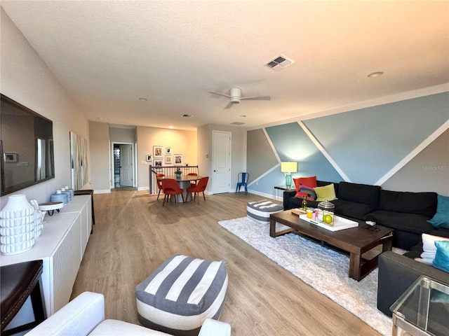 living room featuring ceiling fan, light hardwood / wood-style floors, and a textured ceiling