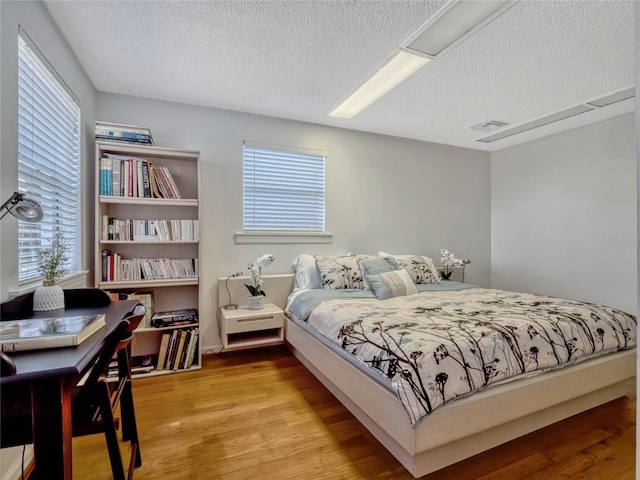 bedroom with visible vents, a textured ceiling, and wood finished floors