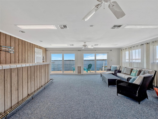 living room featuring carpet floors, visible vents, wooden walls, and a ceiling fan