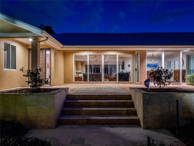 exterior entry at night featuring a patio and stucco siding