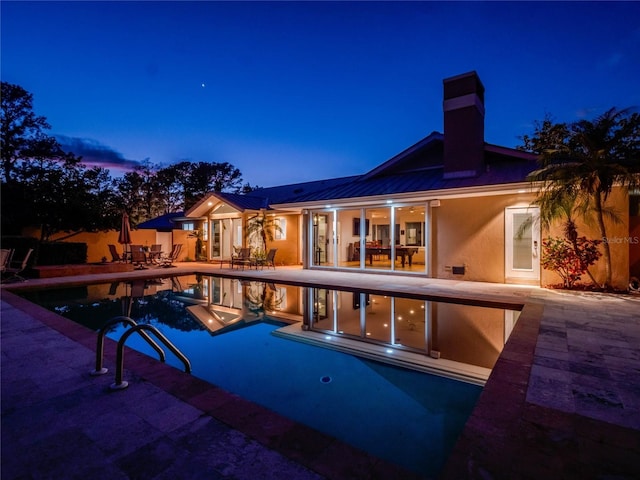 pool at dusk featuring an outdoor pool and a patio