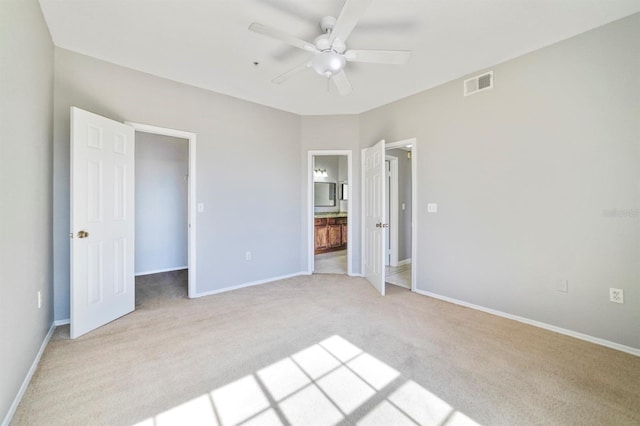 unfurnished bedroom with ceiling fan, a spacious closet, light carpet, and ensuite bath