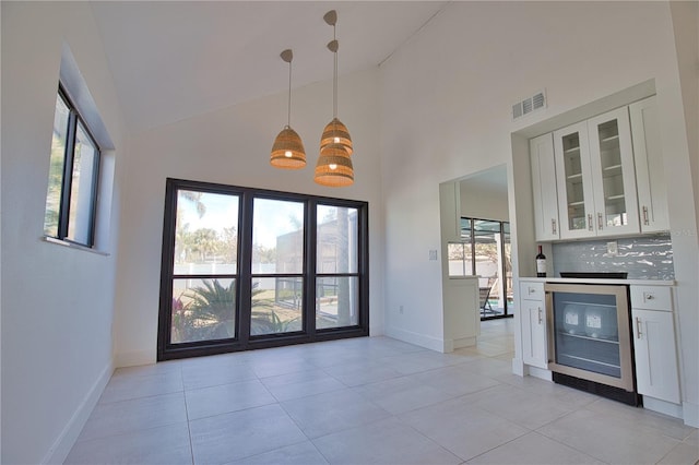 interior space featuring pendant lighting, high vaulted ceiling, wine cooler, white cabinets, and decorative backsplash