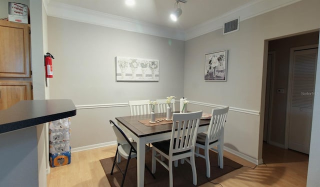 dining area with rail lighting, ornamental molding, and light hardwood / wood-style floors