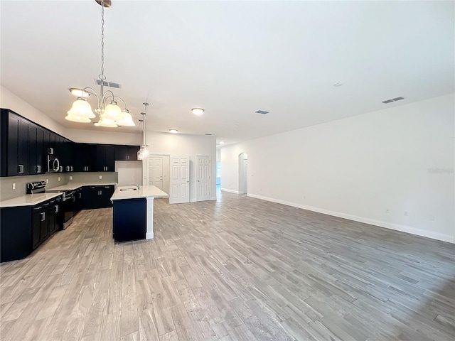 kitchen featuring pendant lighting, appliances with stainless steel finishes, light hardwood / wood-style floors, and a center island with sink