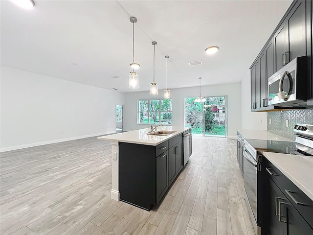 kitchen with sink, a center island with sink, appliances with stainless steel finishes, pendant lighting, and light hardwood / wood-style floors
