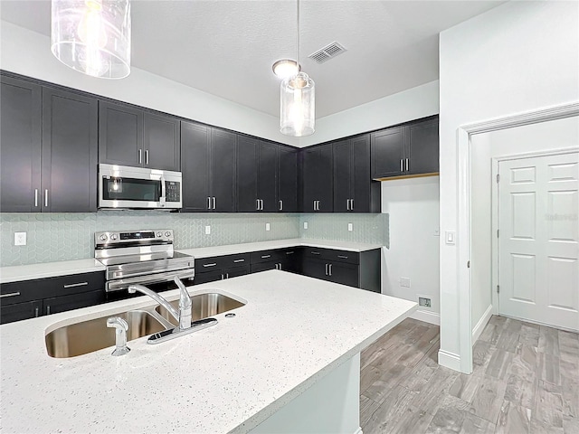 kitchen featuring pendant lighting, sink, stainless steel appliances, light stone countertops, and light hardwood / wood-style flooring