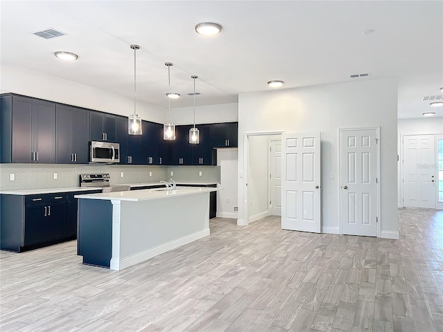 kitchen featuring hanging light fixtures, a center island with sink, light wood-type flooring, appliances with stainless steel finishes, and decorative backsplash