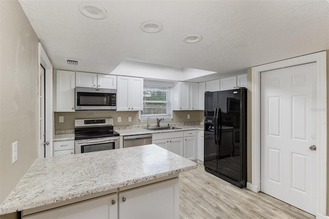 kitchen featuring visible vents, white cabinets, stainless steel appliances, light wood-style floors, and a sink