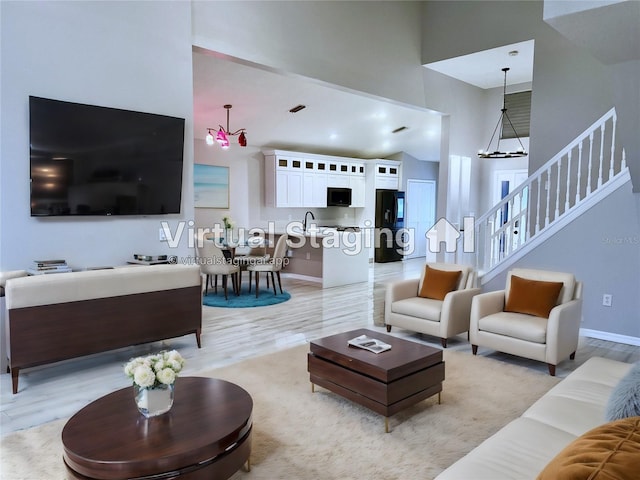 living room with a notable chandelier, a towering ceiling, sink, and light wood-type flooring