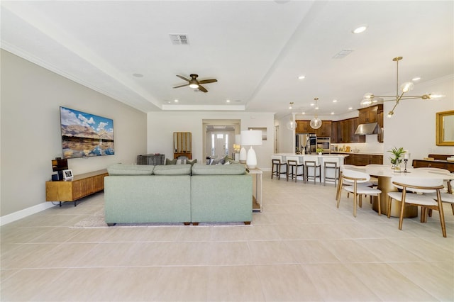 tiled living room featuring a tray ceiling and ceiling fan with notable chandelier