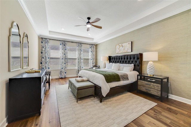 bedroom with hardwood / wood-style flooring, ornamental molding, ceiling fan, and a tray ceiling