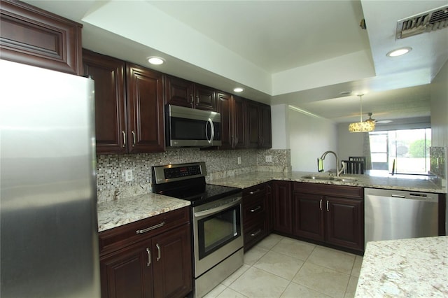 kitchen with a raised ceiling, tasteful backsplash, sink, hanging light fixtures, and stainless steel appliances