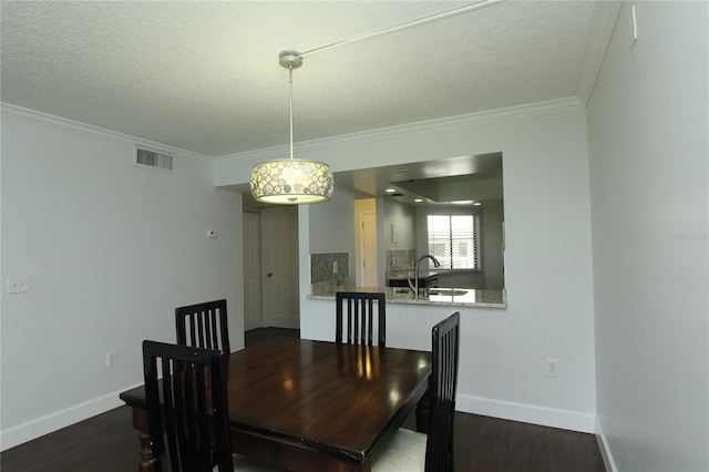 dining room with sink, crown molding, dark wood-type flooring, and a textured ceiling