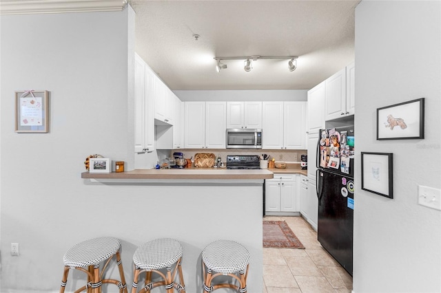 kitchen with a breakfast bar area, kitchen peninsula, white cabinets, and black fridge