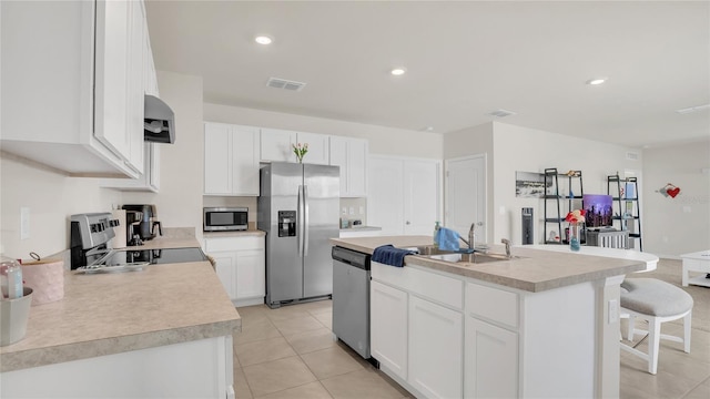 kitchen with sink, light tile patterned floors, stainless steel appliances, white cabinets, and a center island with sink