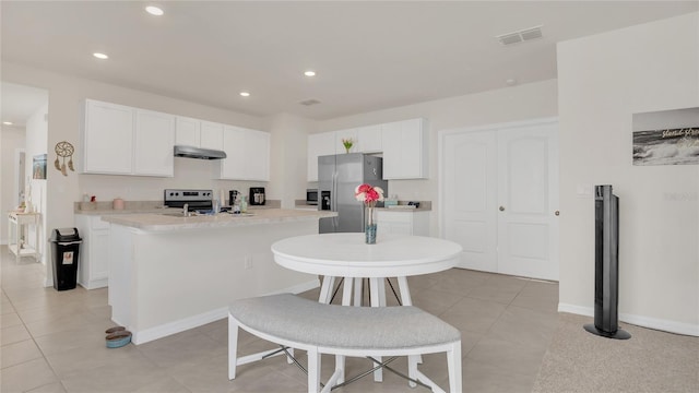 kitchen with white cabinetry, appliances with stainless steel finishes, light tile patterned flooring, and a kitchen island with sink