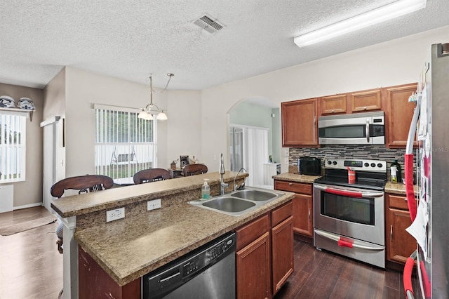 kitchen with pendant lighting, an island with sink, sink, dark hardwood / wood-style flooring, and stainless steel appliances